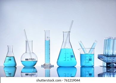 Laboratory glass chemical containers full of blue liquid on glass table isolated. Horizontal composition. Front view