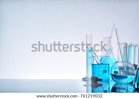 Laboratory glass chemical containers full of blue liquid on glass table isolated. Horizontal composition. Front view