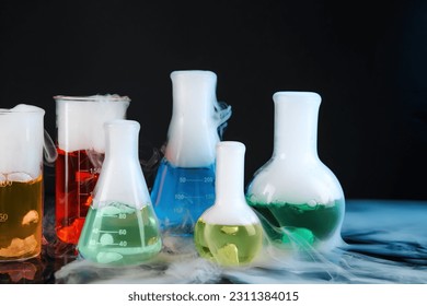 Laboratory glassware with colorful liquids and steam on black background. Chemical reaction