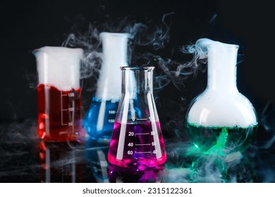 Laboratory glassware with colorful liquids and steam on black background. Chemical reaction