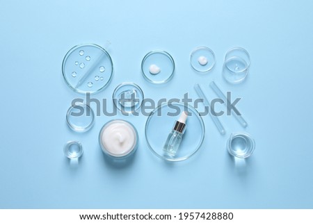 Laboratory glassware and natural ingredients for organic cosmetic product on light blue background, flat lay