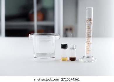 A laboratory glassware set for Thin Layer Chromatography (TLC) including a developing tank, sample solution vials, and a graduated cylinder with 10 ml of solvent.
