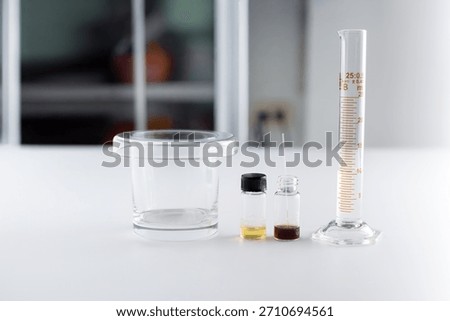 A laboratory glassware set for Thin Layer Chromatography (TLC) including a developing tank, sample solution vials, and a graduated cylinder with 10 ml of solvent.