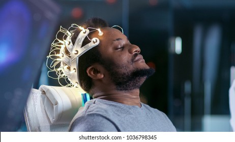 In Laboratory Man Wearing Brainwave Scanning Headset Sits in a Chair with Closed Eyes. Monitors Show EEG Reading and Graphical Brain Model. In the Modern Brain Study/ Neurological Research Laboratory.