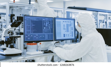 In Laboratory Over The Shoulder View Of Scientist In Protective Clothes Doing Research On A Personal Computer. Modern Manufactory Producing Semiconductors And Pharmaceutical Items.