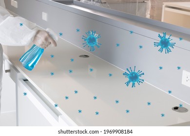 A Laboratory Personal In A White Protective Suit Using Liquid Chemical To Disinfect A Work Bench. 