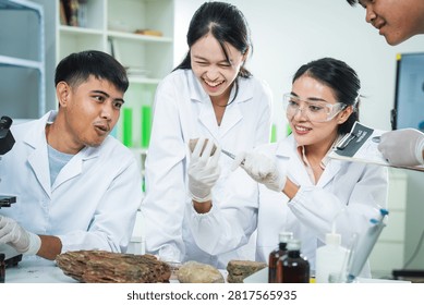 Laboratory scientist student microscope specimen glove eyewear research education Asian, young team smiling during biology experiment with rock sample in modern classroom lab