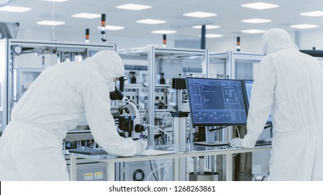 In Laboratory Scientists in Protective Clothes Doing Research, Using Microscope and Entering Data into Personal Computer. Modern Manufactory Producing Semiconductors and Pharmaceutical Items.