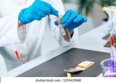 Laboratory Soil Analysis. Female scientist in white coat measuring PH of soil sample with litmus strips. Agrochemical examination of soil. - Powered by Shutterstock