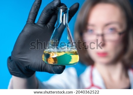Laboratory technician with test tube. Laboratory technician's face is blurred. Girl employee of laboratory. She holds flask towards chamber. Test tube with yellow liquid from chemist.
