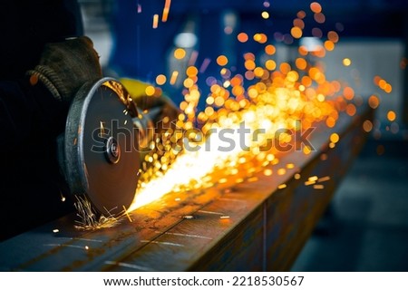 Laborer cuts metal beam with abrasive disk in workshop