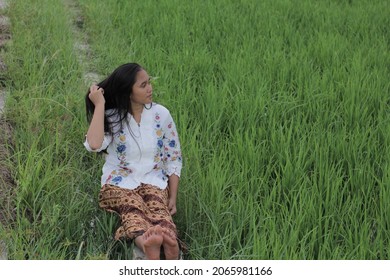 Labuan Bajo, Indonesia - March 05, 2019: A Beautiful And Charming Asian Girl Wearing A White Kebaya And Batik Sarong Is Around The Rice Fields.