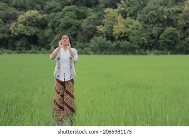 Labuan Bajo, Indonesia - March 05, 2019: A Beautiful And Charming Asian Girl Wearing A White Kebaya And Batik Sarong Is Around The Rice Fields.