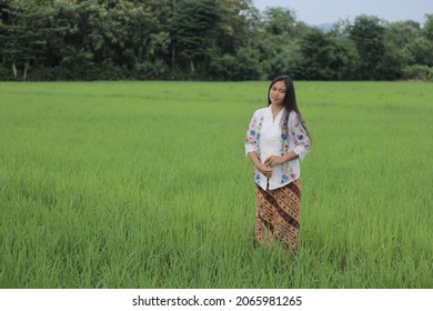 Labuan Bajo, Indonesia - March 05, 2019: A Beautiful And Charming Asian Girl Wearing A White Kebaya And Batik Sarong Is Around The Rice Fields.