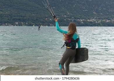 Lac Bourget, Savoie/France 17th July 2020. Wind Boarding And Sailboarding On An Overcast Day. Strong Woman Entering The Lake Holding Kite And Surf Board