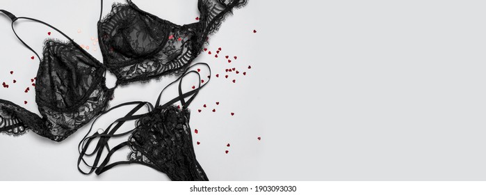 Lace sexy black womens underwear, red heart confetti on gray background flat lay top view copy space. Black lace lingerie. Fashion Concept. Women's bra, panties, erotic clothes. Lingerie advertising