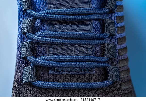 Laced up black blue mesh fabric sneakers macro.
Laced fastening of new sport shoe on a blue background. Elastic
laces of modern textile trainers for active lifestyle, sports and
fitness. Front view.