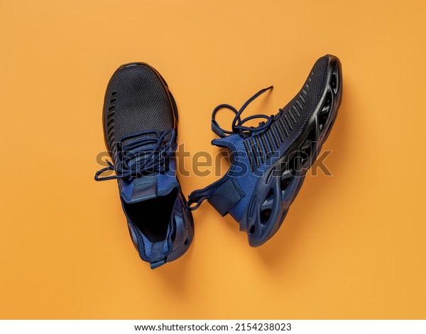 Laced up black blue mesh fabric sneakers over\
orange background. Pair of grooved men shoes for fitness and active\
lifestyle. New fabric sneakers with laced fastening. Sport shoes\
concept. Top view.