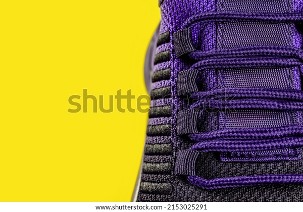 Lacing of purple black textile sneakers against yellow\
background. Laced fastening of new sport shoe close-up. Elastic\
laces of modern mesh sneakers for active lifestyle, fitness and\
sports. 