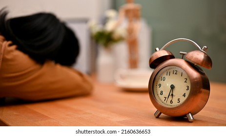 Lack of female office worker sleeping at her office desk, taking an afternoon nap from busy work. Tired woman. vintage clock on worktable.