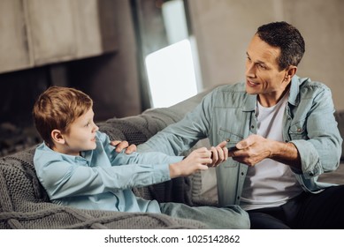 Lack Of Understanding. Strict Young Father Taking Away The Phone From His Sons Hands, Trying To Make His Stop Playing Games, While The Boy Resisting