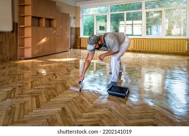 Lacquering parquet floors. Worker uses a roller to coating floors. Varnishing lacquering parquet floor by paint roller - second layer. Home renovation parquet