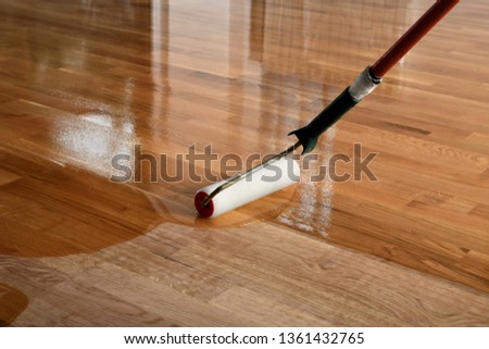 Lacquering wood floors. Worker uses a roller to coating floors. Varnishing lacquering parquet floor by paint roller - second layer. Home renovation parquet