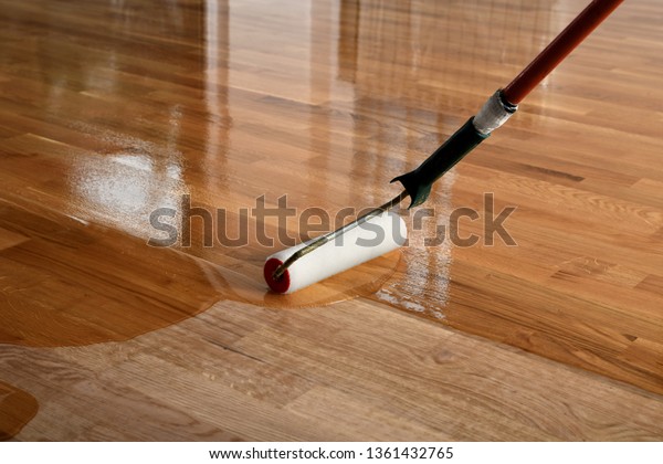 Lacquering wood floors. Worker uses a\
roller to coating floors. Varnishing lacquering parquet floor by\
paint roller - second layer. Home renovation\
parquet