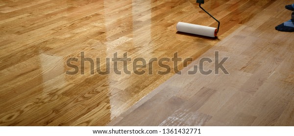 Lacquering wood floors. Worker uses a\
roller to coating floors. Varnishing lacquering parquet floor by\
paint roller - second layer. Home renovation\
parquet