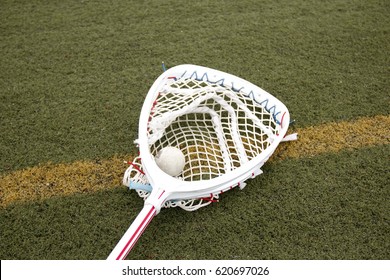 Lacrosse Goalie Stick With A Ball In The Netting On A Green Turf Field