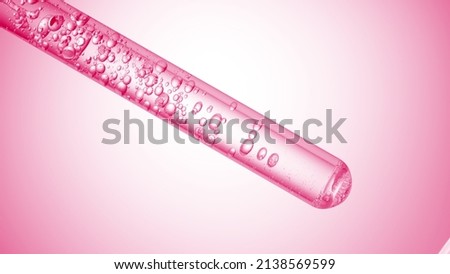 Lactic acid is injected into a test tube with clear liquid creating bubbles on pale pink background. Abstract body care cosmetics with lactic acid formulating the concept