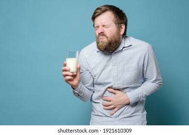 Lactose Intolerance. A Man Holds A Glass Of Milk In His Hand And Suffers From Severe Abdominal Pain. Blue Background.