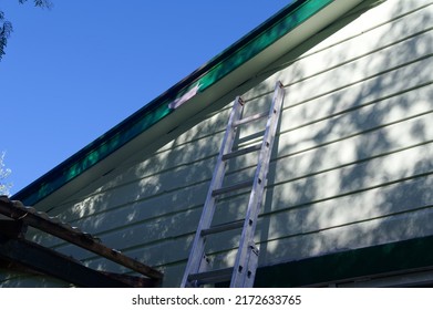 A ladder is leaning against a weatherboard house, perhaps it is there so someone can fix the broken roof at the side