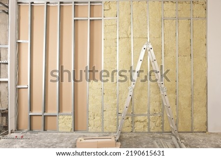 Ladder near wall with metal studs and insulation material indoors