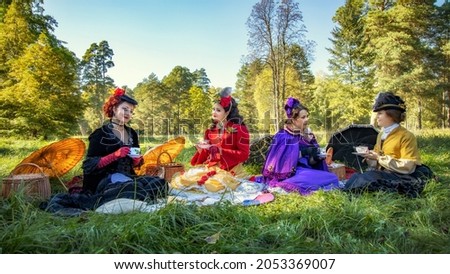 Ladies in 19th century dresses at a picnic hold cups of drinks and chat