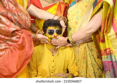 Ladies applying turmeric paste during haldi ceremony. Groom is wearing sun glasses and is smiling 