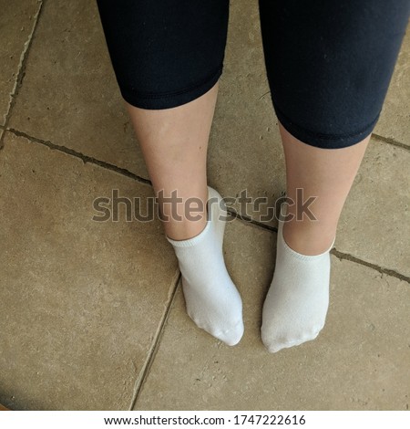 Ladies feet on a tiled floor wearing well worn socks 