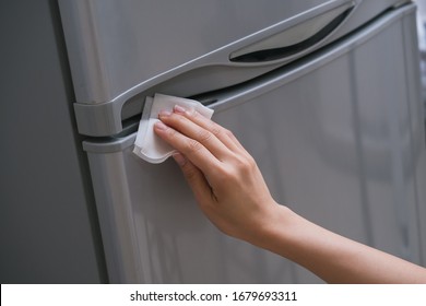 Ladies hand wiping the handle of the fridge door to prevent the spread of bacteria and virus. Personal hygiene concept. 
