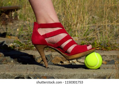 Ladies Leg - Foot In The Court Shoe And A Tennis Ball.A Woman In A Pump Shoe Standing On A Yellow Tennis Ball. Woman Standing On Overgrown Train Track.