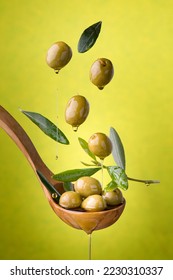 ladle with olives and oil on a green background. Olives, extra virgin olive oil and olive leaves float in the air - Shutterstock ID 2230310337