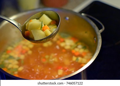 Ladle With Vegetable Soup. Cooking Pot On Background. Focus On Foreground.
