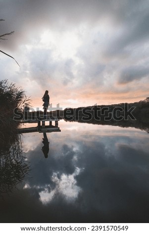 Similar – Image, Stock Photo Lady aged 20-25 standing on a wooden pier by a pond watching the sunset over the town of Oostende, western Belgium. Dramatic red-orange sky