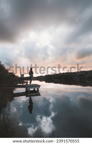 Similar – Image, Stock Photo Lady aged 20-25 standing on a wooden pier by a pond watching the sunset over the town of Oostende, western Belgium. Dramatic red-orange sky