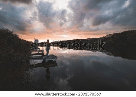 Similar – Image, Stock Photo Lady aged 20-25 standing on a wooden pier by a pond watching the sunset over the town of Oostende, western Belgium. Dramatic red-orange sky