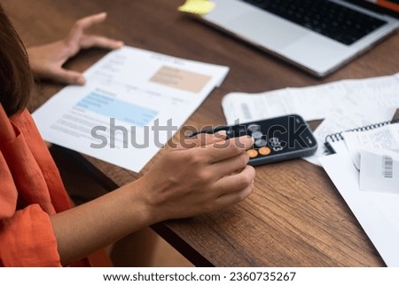 A lady, armed with payment receipts, pays household utility bills online from home using her trusty laptop