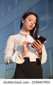 Lady Business Manager Stands Near Office And Chats With Friend. Young Woman In Businesswear Smiles And Straightens Long Dark Hair Behind Ear