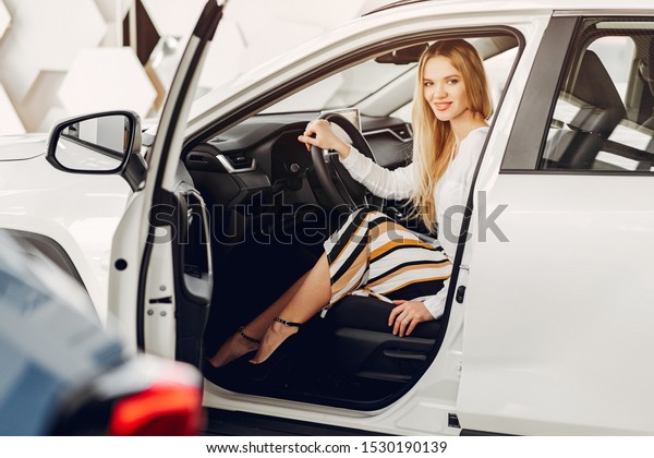 Lady in a car salon. Woman buying the car. Blonde\
in a white shirt