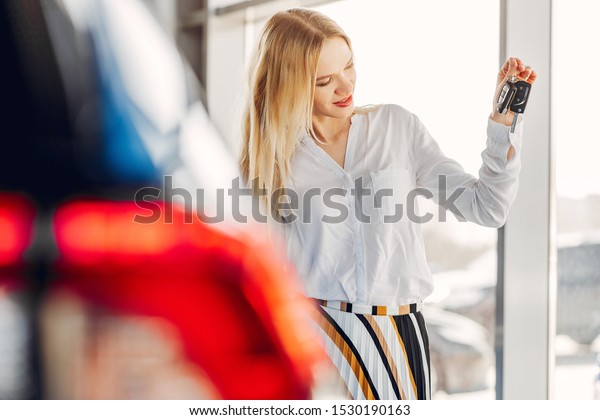 Lady in a car salon. Woman buying the car. Blonde\
in a white shirt