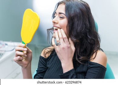 Lady checking teeth in mirror. Young female at dentist office. New dental implants.