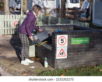 A Lady At A Chemical Waste Point On A Campsite Empties Contents Of Her Portable Cassette Toilet To Clean It.Bottle Of Cleaner On Floor.Chemical Waste Point Sign Visible